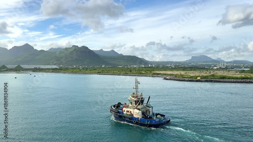 A tugboat works in a busy waterway close to the city harbor. It navigates the water as ships await assistance. Workers are seen on board, managing operations.