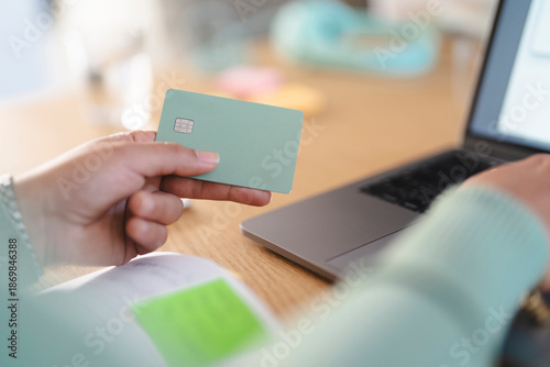 A person holds a payment card near a laptop, ready to make an online transaction.
