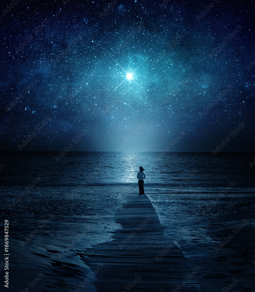 Fototapeta premium Girl facing the ocean under a luminous star in a deep night sky. Mystical, spiritual, cosmic atmosphere with water reflection and celestial light. Elements of this image furnished by NASA