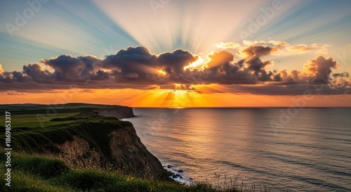 Coastal cliffs at sunset, sun rays piercing clouds over serene ocean
