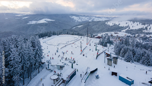Aerial view of a small resort on top of the mountain in winter season at sunset. Photography was shot from a drone at a higher altitude. Aerial view of a resort in winter at sunset