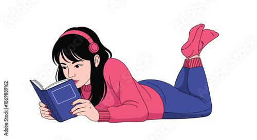 Young woman lying comfortably on her stomach reading a blue book while wearing pink headphones and matching cozy sweater and socks.