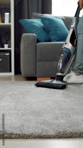 A person is vacuuming a carpet in a living room during the day using a home appliance.