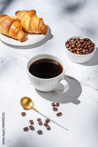 Freshly brewed black coffee in a cup on a white marble background with croissants