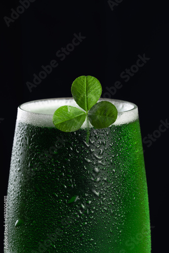 Close up of chilled green beer glass decorated with a shamrock leaf and condensation drops against a black background
