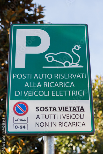 Italian road sign indicating parking spaces reserved for electric vehicle charging, with no stopping allowed for non-charging vehicles. Concept of electric mobility and sustainable transportation.