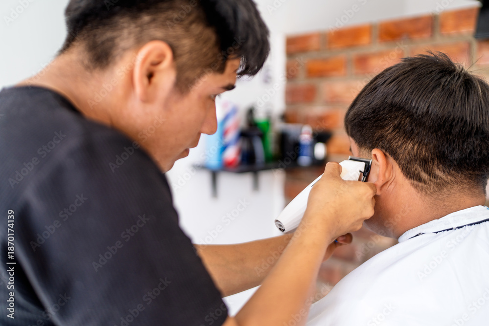 Fototapeta premium Latino barber cutting customer's hair in barbershop