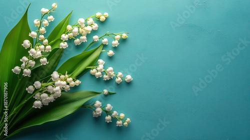 Delicate white lily of the valley flowers with lush green leaves arranged diagonally on a textured turquoise background conveying freshness and simplicity