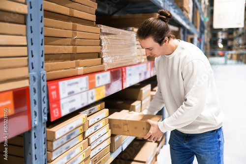 Canvas Print Young man picking a flat cardboard box from a shelf in a self-service furniture warehouse store