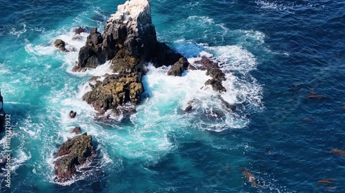 Powerful ocean waves crash against rugged coastal rocks, creating swirling turquoise water and white foam in a dramatic natural seascape.