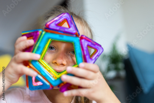 Young girl playing with colorful magnetic building tiles at home and holding star near face