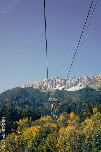 Cable car travels over trees and mountains during a sunny day in the fall season