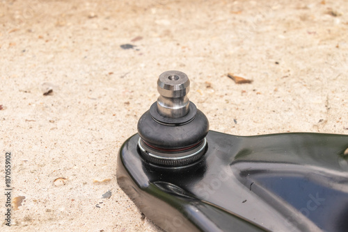 Close-up of a car suspension ball joint on a textured concrete surface.