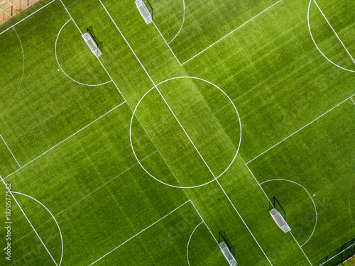 Top-down aerial view of a green football field with white markings and goals. Clean geometric composition, symmetry and texture, outdoor sports and soccer training concept