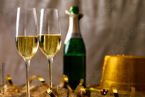 Closeup of champagne in flutes with golden ribbon by bottle on table
