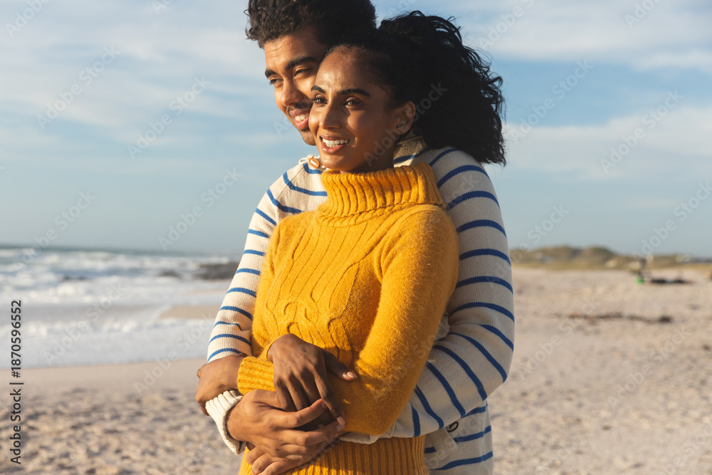 Naklejka premium Happy multiracial couple embracing each other while looking away at beach against sky