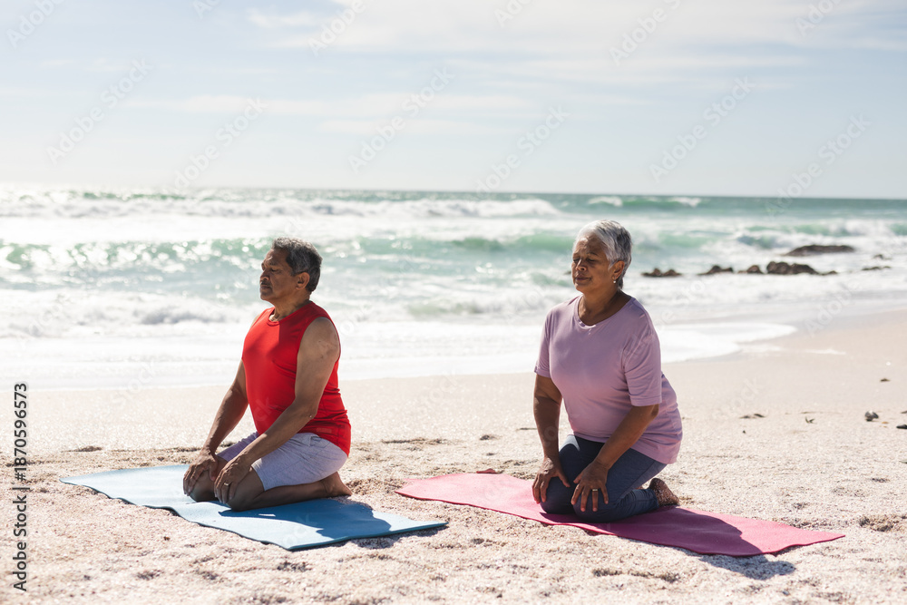 Fototapeta premium senior couple meditating while kneeling on yoga mats at beach against sky during sunny day