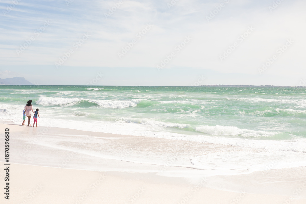 Naklejka premium Full length of multiracial mother and children enjoying sunny weekend on shore at beach