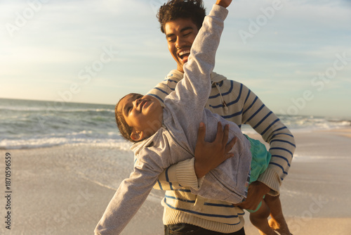 Obraz na plátně Cheerful man carrying daughter pretending to fly at beach against sky on sunny d