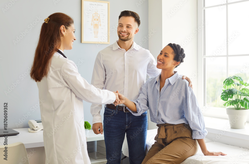 Fototapeta premium A female family doctor greets a smiling couple in a sunlit clinic, offering reassurance while reviewing checkup results and follow-up care. Couple shaking hands with physician in medical clinic.