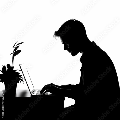 Silhouette of a person working intently on a laptop at a desk with a plant.
