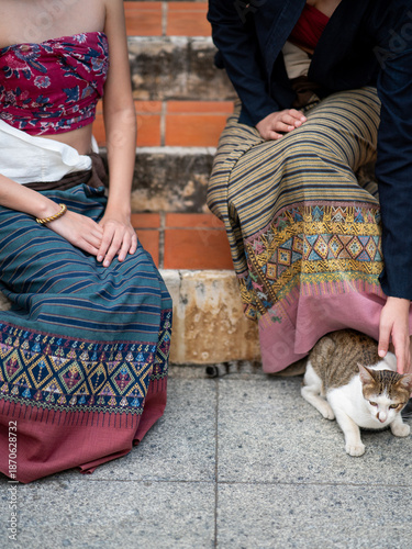 Modern women wearing traditional Lanna clothing sitting on temple steps with a cat