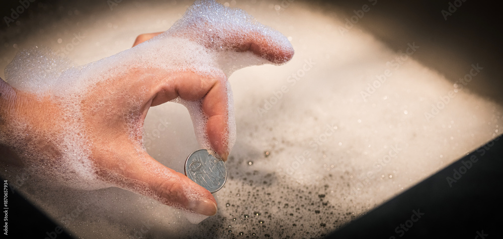 Fototapeta premium Hand Holding Coin in Pinched Fingers Gesture Over Foamy Sink — Money Laundering Concept