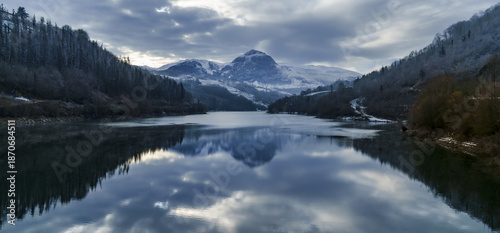 The majestic peak of Txindoki emerges from the winter clouds above the cold waters of the Ibiur reservoir.