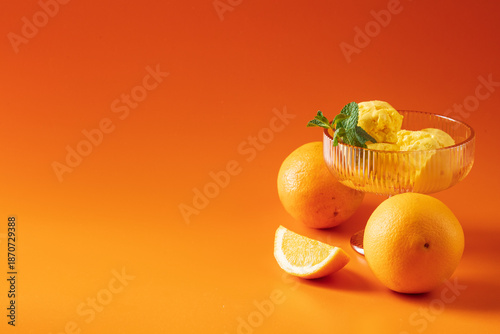 Tableau sur toile Orange sorbet in a glass bowl, arranged on a vibrant orange background with copy space