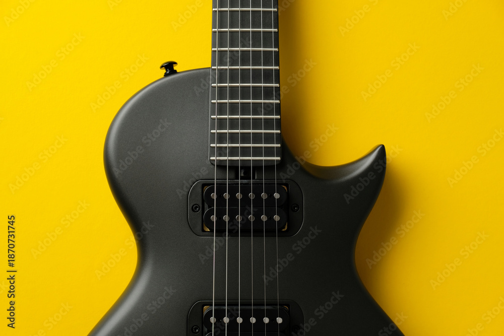 Fototapeta premium Symmetrical close-up of a black electric guitar body on a yellow background
