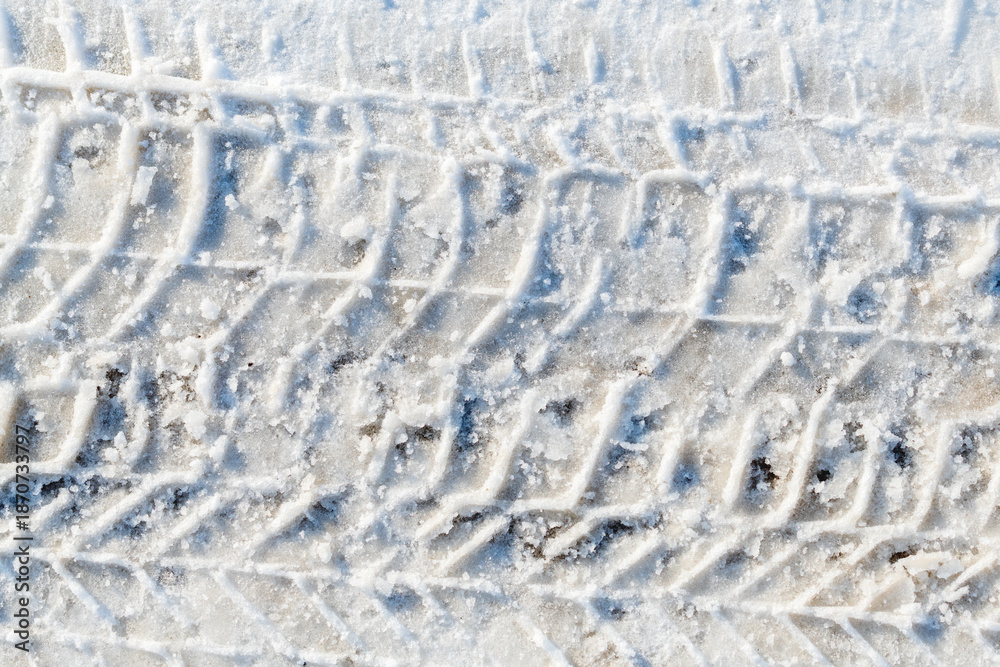 Obraz premium Car tire tracks forming a repeating pattern in fresh white snow, top view winter background with minimal texture and strong graphic lines. Directly above.