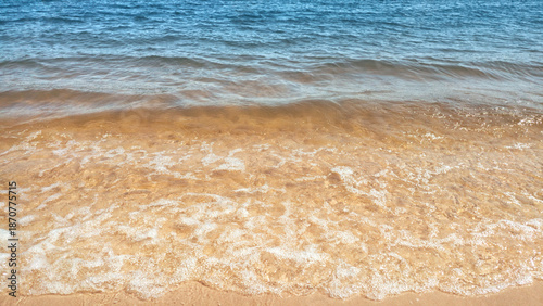The lake water waves with foam on the yellow sand beach. The summer mood backdrop.