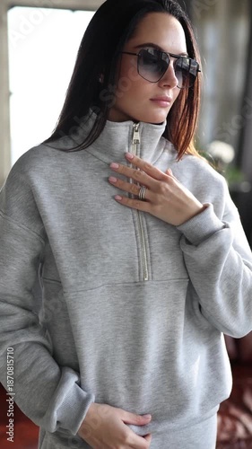 Young woman in grey fleece tracksuit and sunglasses posing in studio