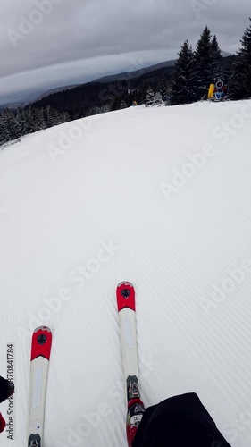 Travel and winter adventure concept. Beautiful POV ski landscape on the mountains. Skier skis down a snowy mountain trail in cloudy weather. Vertical shot