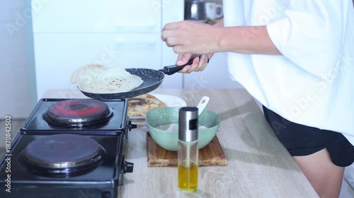 A person expertly flips a pancake in a skillet and slides it onto a plate with others, completing the cooking process with a satisfying final touch.