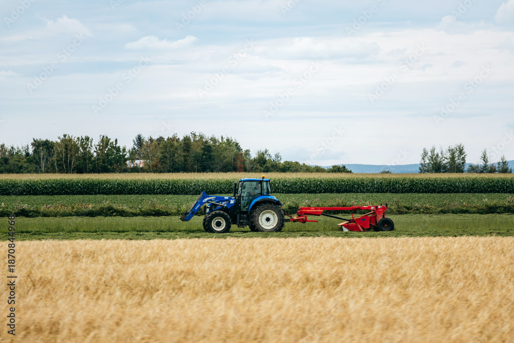 Fototapeta premium Saint-Gedeon, Canada - August 19, 2025: Tractor working in agricultural field during summer harvest season