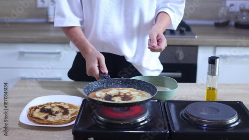 A person flips a golden-brown pancake in a skillet and slides it onto a growing stack on a plate, showcasing the final step in a perfect pancake-making routine.