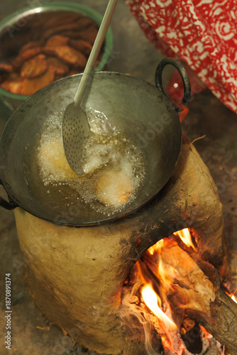 Indian rural woman cooking traditional festival sweet like thekua gulgule jalebi during diwali holi chhat puja pooja on mud chulha stove with vibrant flames