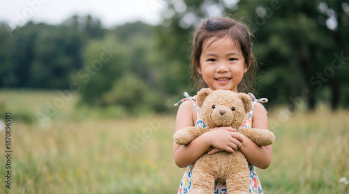 Portrait Happy child girl with to her teddy bear friend outdoors on green grass lawn. An Asian girl hugs a teddy bear. Friendship concept, childhood
