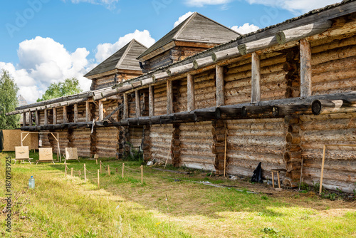 The impressive wooden walls of a reconstructed Old Slavic fortress, made of round, hewn logs. Old barracks and boyar chambers. A bright, sunny day.