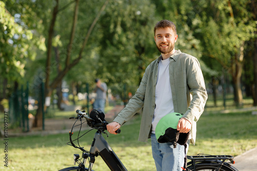 Wallpaper Mural Man stands with bicycle in park smiling while holding a green helmet near trees on a sunny day Torontodigital.ca