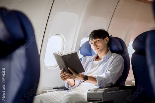 A businesswoman relaxes in her airplane seat, finding satisfaction and quiet contemplation while reading literature during a long vacation flight.