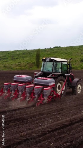Agricultural tractor with seed drill is actively planting seeds in a plowed field, showcasing the planting process and soil disturbance as the machine moves forward