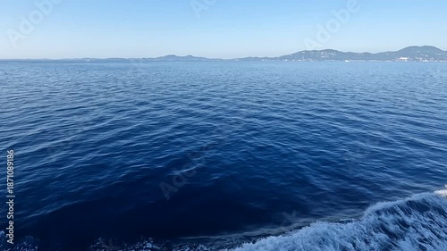 Expansive deep blue ocean with gentle ripples and distant coastal hills under clear sky.