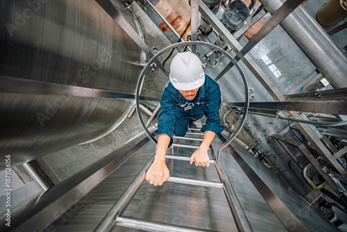 Top view male worker climbs up the ladder inspection stainless tank work at height