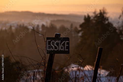 Strasse an einem Weinberg bei Sonnenaufgang im Winter, ein handgeschriebenes Schild wirbt für den Verkauf von Essig ab Hof