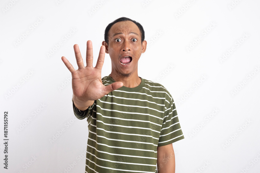 Naklejka premium An Asian wearing a green shirt with white stripes holds up his hand with his palm facing forward, signaling to stop, with a surprised and alert expression. 