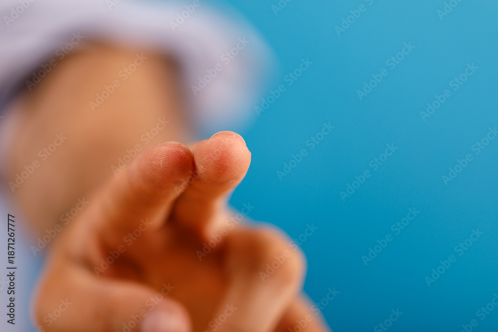 Obraz premium Human hand pointing, gesture of choosing, focus or selecting. Blue backdrop with soft focus in the background. Concept of direction, decision, a