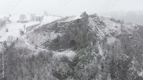 Aerial drone footage pushing forward toward Thor's Cave in Derbyshire, England, showing snow covered cave entrance, suitable for travel, tourism, nature and establishing shot use.