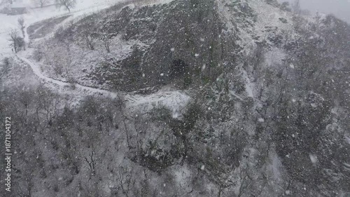 Aerial drone footage pushing forward and panning up at Thor's Cave in Derbyshire, England, revealing snow covered cave entrance for travel, tourism, nature and establishing shot use.